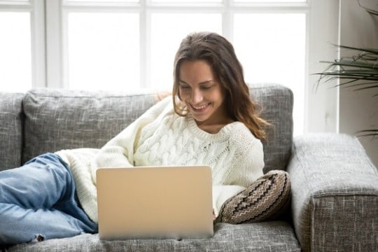 Smiling woman relaxing on couch with laptop